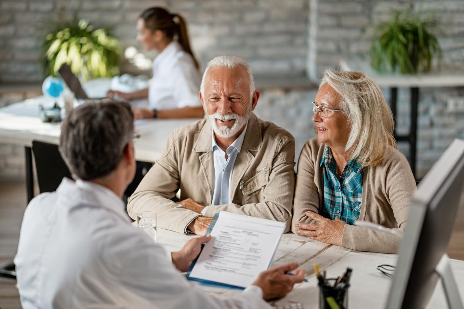 happy-senior-couple-communicating-with-doctor-about-their-health-insurance-while-going-through-paperwork-compressed